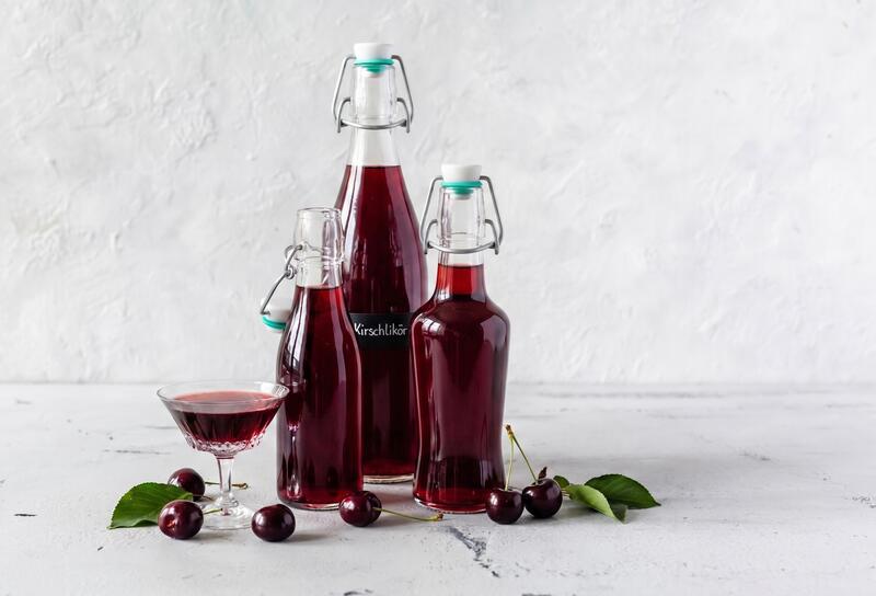 Drei Flaschen mit rotem Likör, daneben ein Glas und ein paar Kirschen