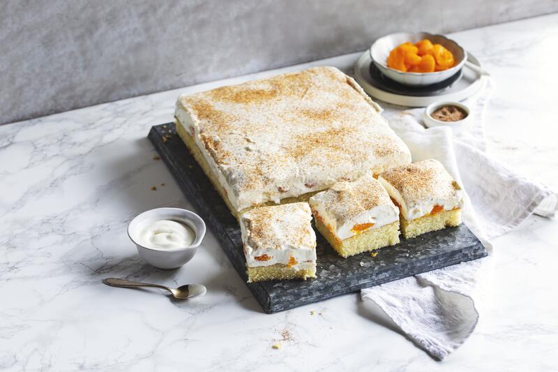 Angeschnittener rechteckiger Fantakuchen mit Schmand vom Blech auf hellem Untergrund