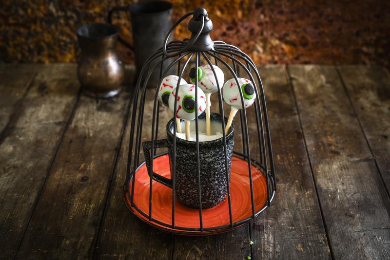 Dekorierte Cake-Pops mit Augen unter einem Käfig mit Halloweendekoration