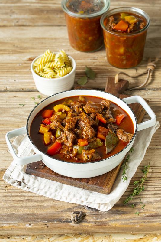 Fleisch und Paprika in einem Schmortopf angerichtet auf einem Holzbrett.