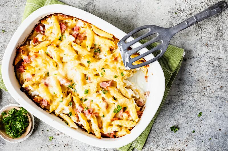 Auflaufform und Teller mit Nudel-Schinken-Gratin