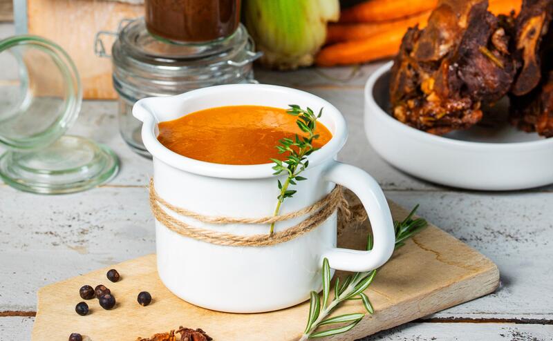 Bratensoße in weißem Soßenkännchen auf Holzbrett