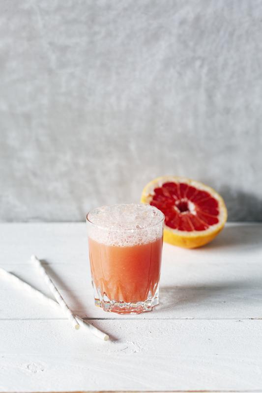 Grapefruitsaft im Glas mit Strohhalm und halber Grapefruit