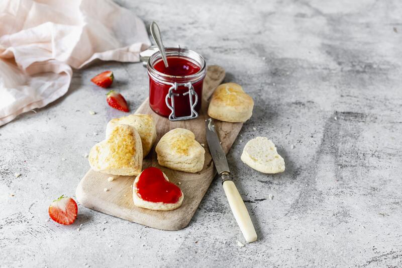 Scones in Herzform auf kleinem Holzbrett mit Marmeladenglas