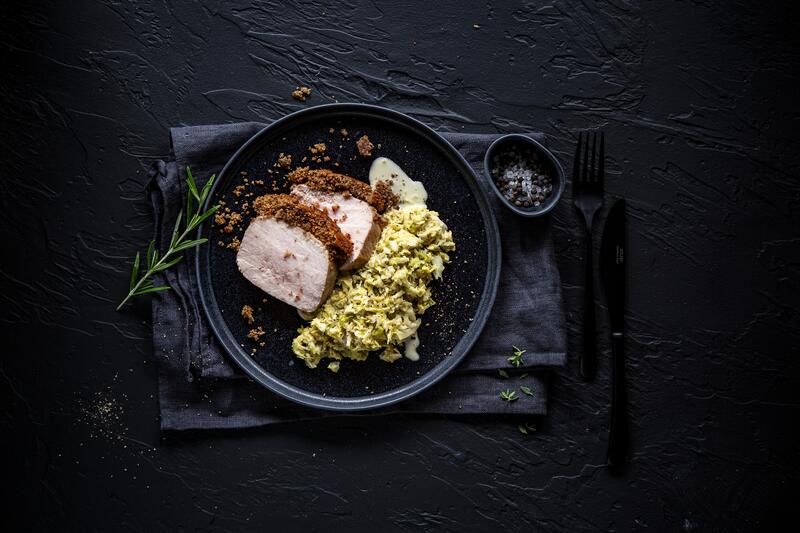 Schweinebraten mit Knusperkruste auf schwarzem Teller