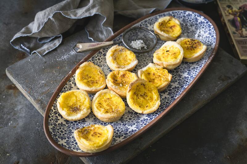 Elf Pastéis de Nata aus dem Thermomix® auf länglichem blau-gemusterten Teller