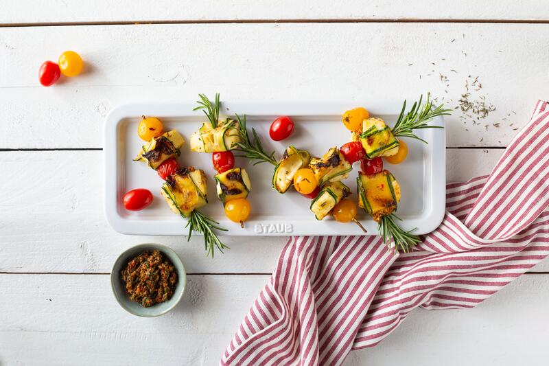 Länglicher weißer Teller mit Halloumi-Gemüse-Spießen mit Rosmarin