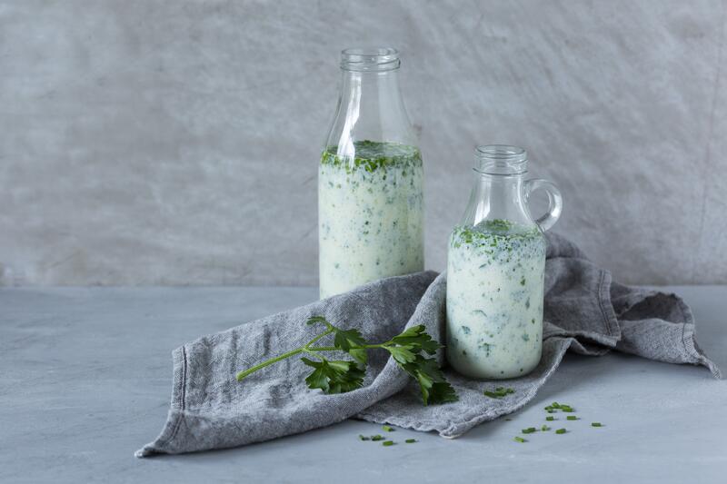 Zwei Flaschen mit Joghurt-Kräuter-Dressing aus dem Thermomix® in grauer Welt