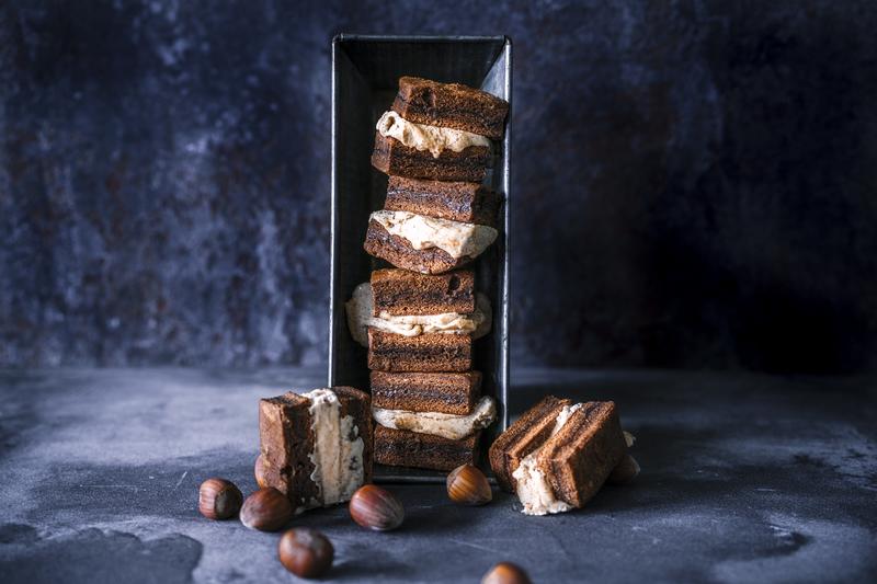 Aufgestellte Kastenform mit gestapelten Kaffeebrownie-Sandwiches aus dem Thermomix® auf dunklem Untergrund