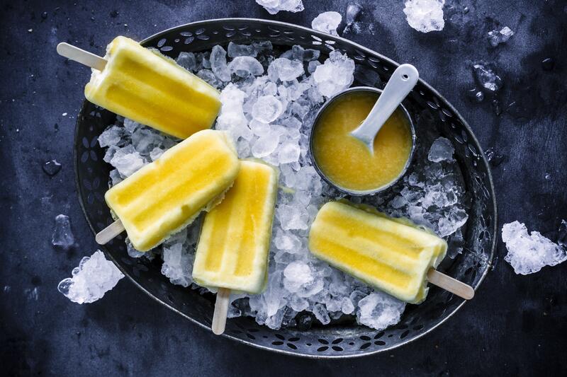 Vier gelbe Solero-Eis am Stiel aus dem Thermomix® in dunkler ovaler Schale mit Eiswürfeln