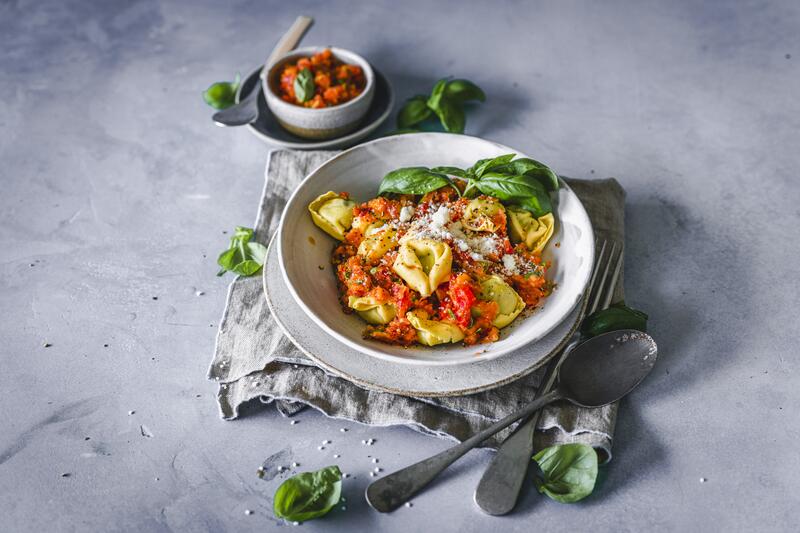 Tortellini mit Tomate und Basilikum auf einem Teller.