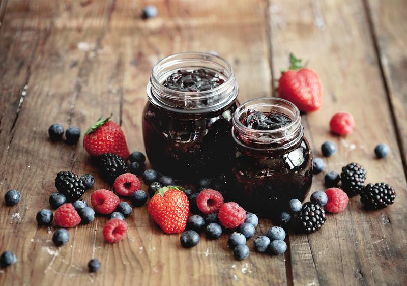 Zwei Marmeladengläser mit Mehrfruchtgelee aus dem Thermomix auf Holzuntergrund mit angelegten Beeren