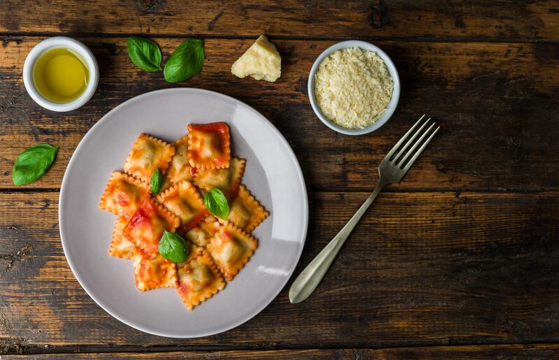 Ravioli in Tomatensoße auf einem weißen Teller mit Basilikum garniert