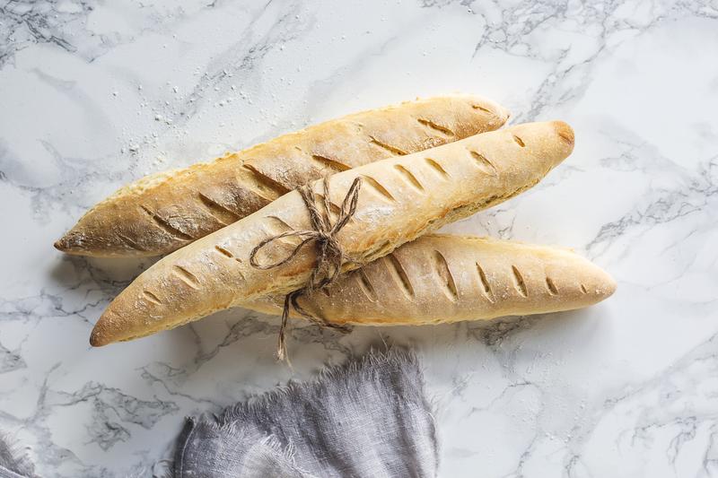 Drei klassische Baguettes auf grau-meliertem Untergrund von oben fotografiert