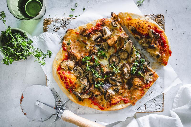 Ovale Pizza Funghi auf weißem Backpapier von oben fotografiert