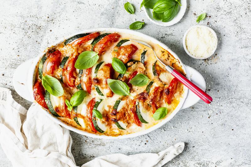 Ovale weiße Auflaufform mit Gemüseauflauf aus Tomaten, Mozzarella und Zucchini von oben fotofrafiert