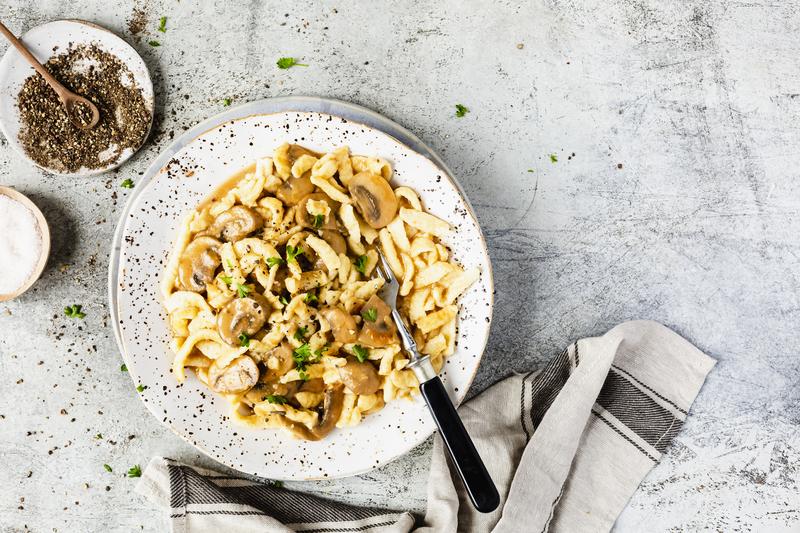 Heller Teller mit Spätzle und Järgersoße aus dem Thermomix® auf hellgrauem Untergrund