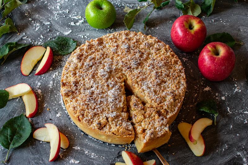 Apfelkuchen mit Streusel auf dunklem Untergrund von Äpfeln umgeben