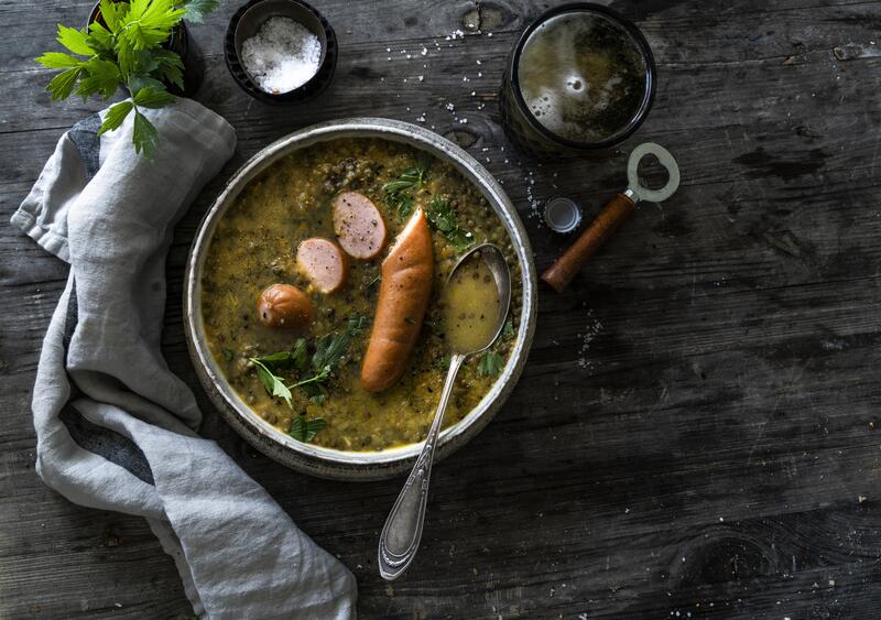 Tiefer Teller mit Linsensuppe mit Bockwurst auf dunklem Untergrund