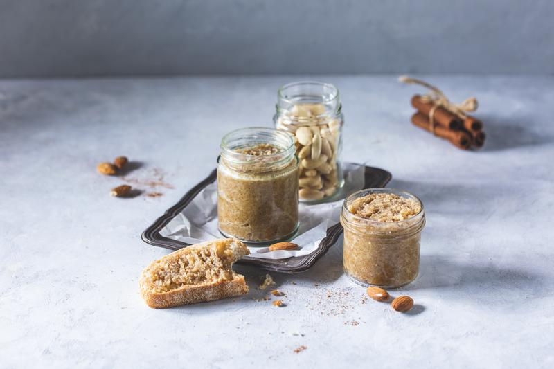 Ein Glas mit Mandeln, zwei kleine Gläser mit Marzipancreme mit angelegter Baguettescheibe