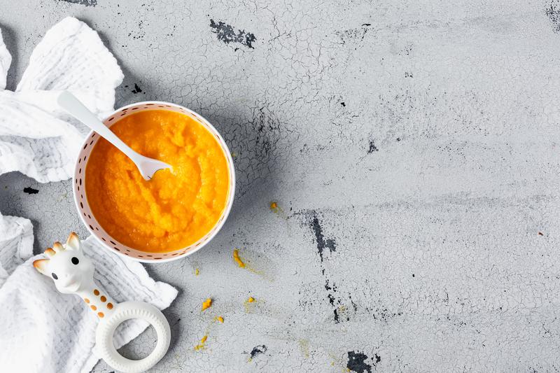 Schale mit Karottenbrei und Babylöffel auf grauem Untergrund