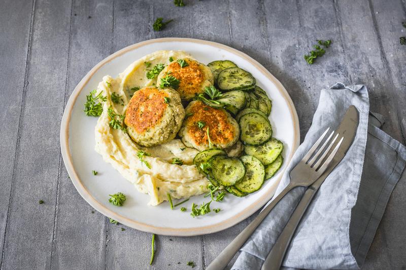 Weißer runder Teller mit Fischfrikadellen auf Püree und Gurkensalat