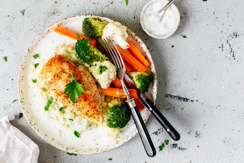 Runder Teller mit Hähnchenbrust und buntem Gemüse auf Reis mit angestelltem Salz