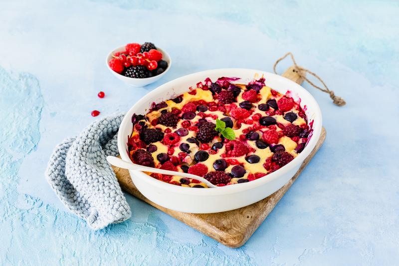 Ovale weiße Auflaufform mit Quarkauflauf mit Beeren auf Holzbrettchen