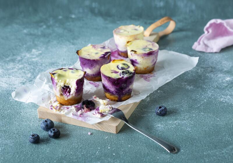 Fünf Käsekuchenmuffins mit Blaubeeren auf weißem Backpapier