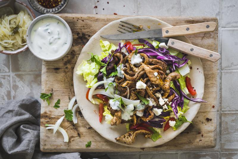 Teller mit Fleisch und Salat auf Holzbrett