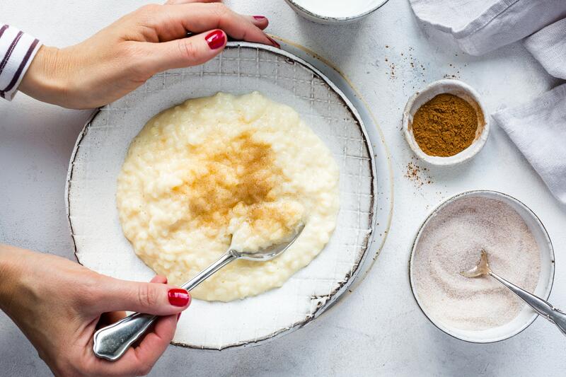 Milchreis mit Vanillepudding auf einem hellen Teller, daneben Zucker und Zimt in Schälchen