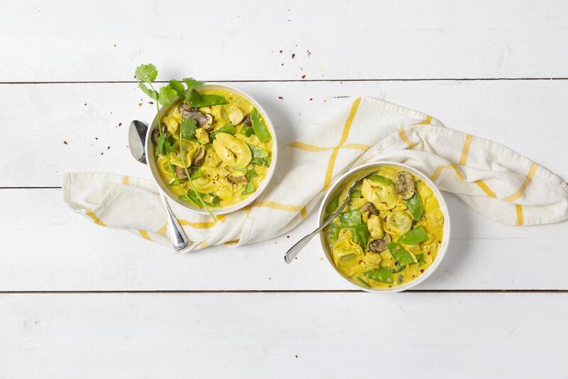 Zwei Schüsseln mit Tortellini mit Hähnchen und Currygemüse mit frischen Kräutern