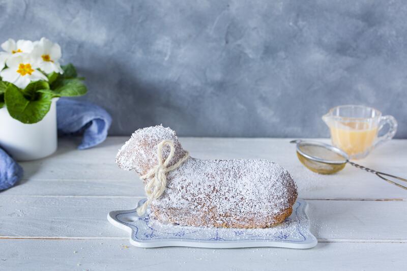 Osterlamm mit Puderzucker bestäubt, daneben ein kleines Sieb und Likör in einer Karaffe