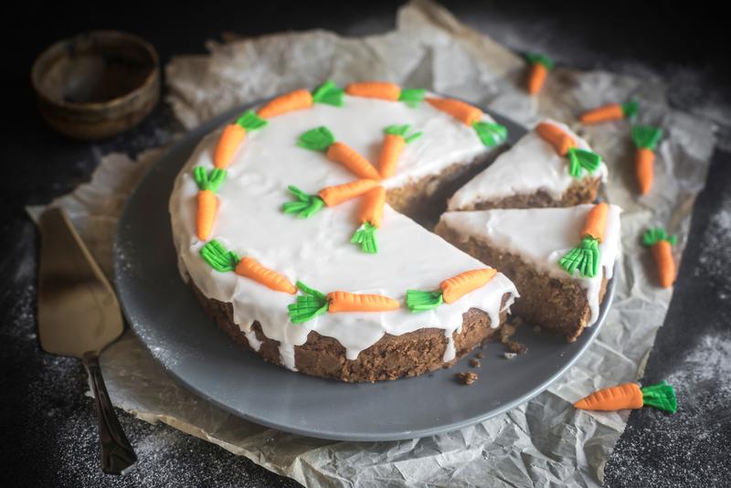 Runder Zucchini-Karotten-Kuchen mit Zuckerguss und Dekor-Karotten verziert, zwei Stücken herausgeschnitten
