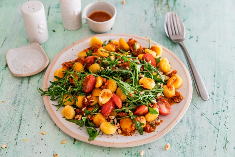 Gnocchi mit roter Soße, Tomaten und Rucola auf weißem Teller mit Besteck