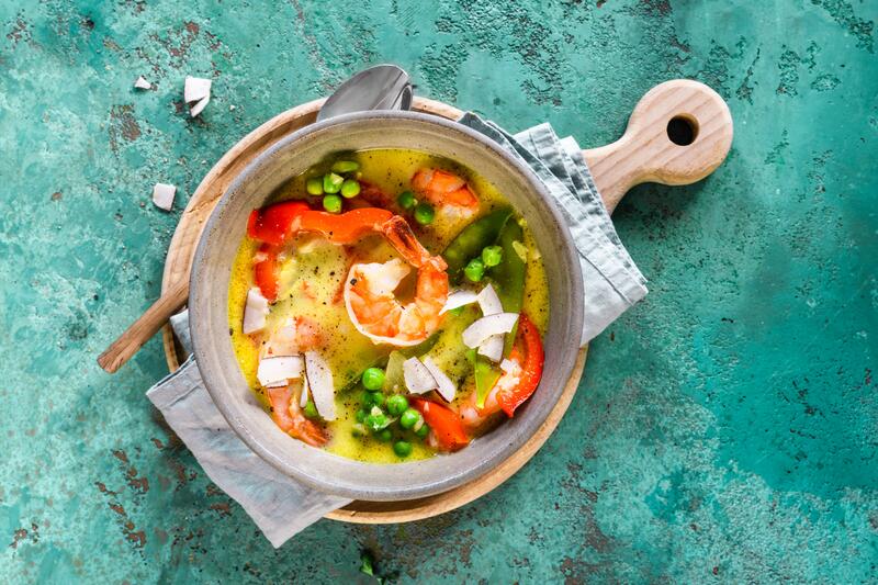 Tiefer Teller mit Kokossuppe mit Paprika und Erbsen auf blau-grünem Untergrund
