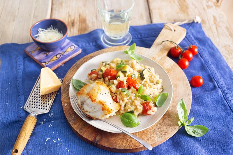 Weißer Teller auf rundem Holzbrett mit Risotto und Kabeljaufilet