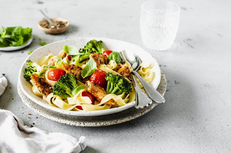 Weißer Teller mit breiten Bandnudeln, Hähnchen, Tomaten und Brokkoli