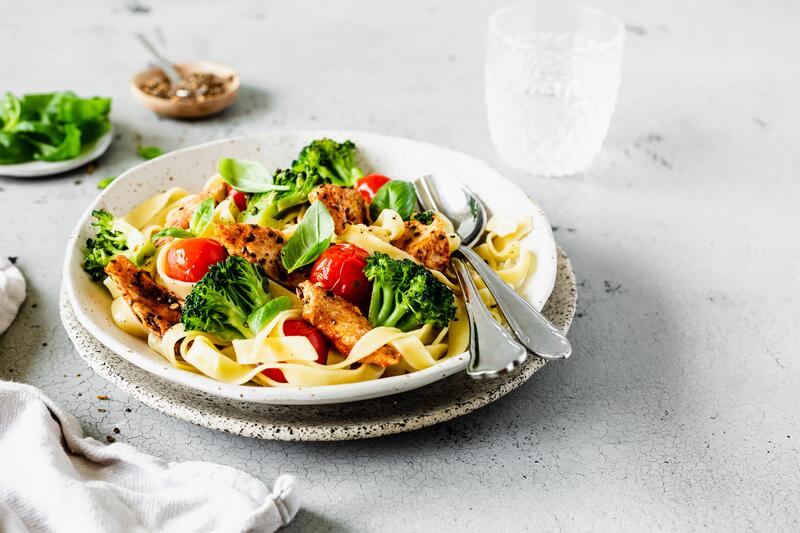 Weißer Teller mit breiten Bandnudeln, Hähnchen, Tomaten und Brokkoli
