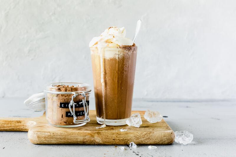 Eiskaffee in großem Glas mit angestelltem Eiskaffeepulver auf Holzbrett