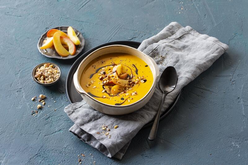 Kürbissuppe mit Äpfeln und Haselnüssen auf grauem Hintergrund