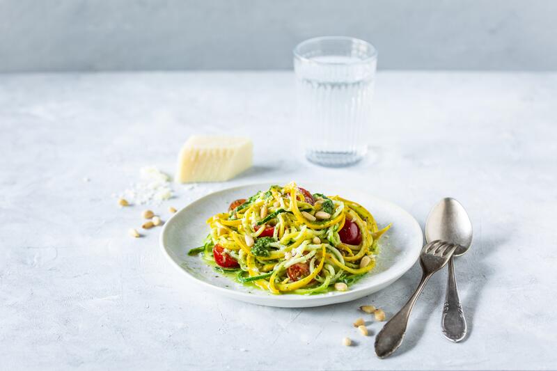 Zoodles auf weißem Teller mit Wasserglas Besteck und Käsestück