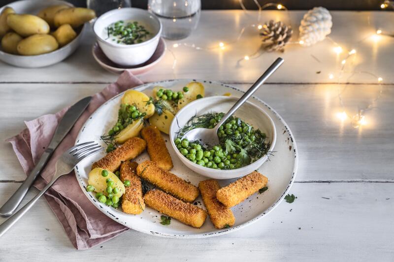 Runder weißer Teller mit veganen Fischstäbchen, Kartoffeln und Erbsen