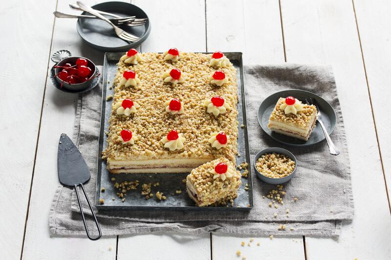 Blechkuchen mit gehackten Nüssen, heller Creme und Kirschen