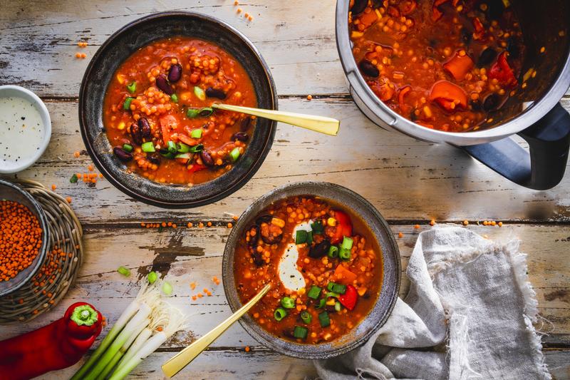 Zwei Schüsseln und ein Topf mit Chili mit roten Linsen auf Holztisch
