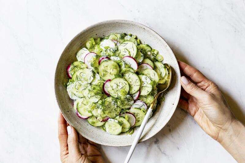 Gurkensalat in einer Schüssel mit zwei Händen und Löffel
