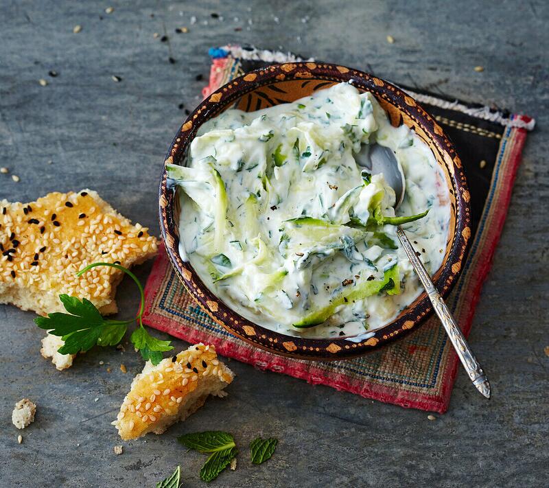 Joghurt-Dip mit Zucchini in Schüssel neben Sesambrot