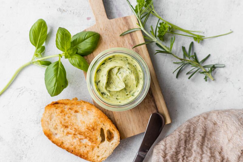 Kräuterbutter in kleinem Glas auf Holzbrett mit angelegten Brotscheiben