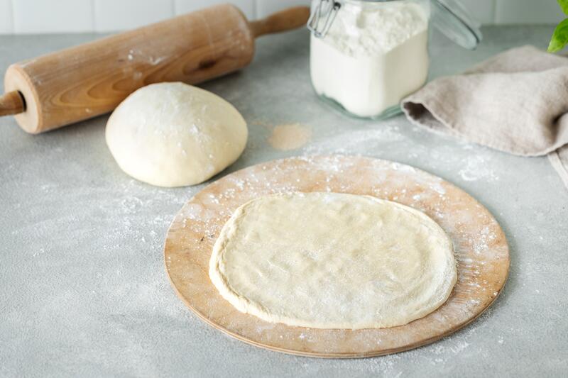 Rund ausgerollter Pizzateig auf rundem Holzbrett