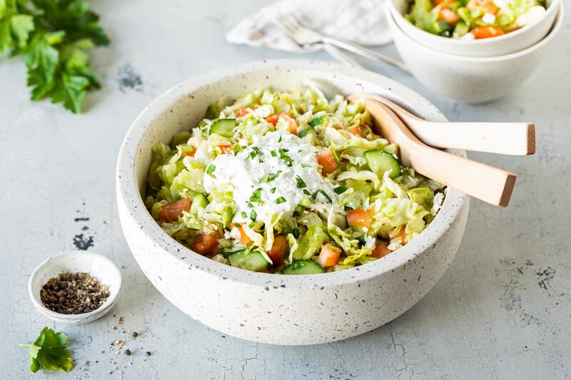 Griechischer Eisbergsalat in großer Salatschüssel mit Salatbesteck